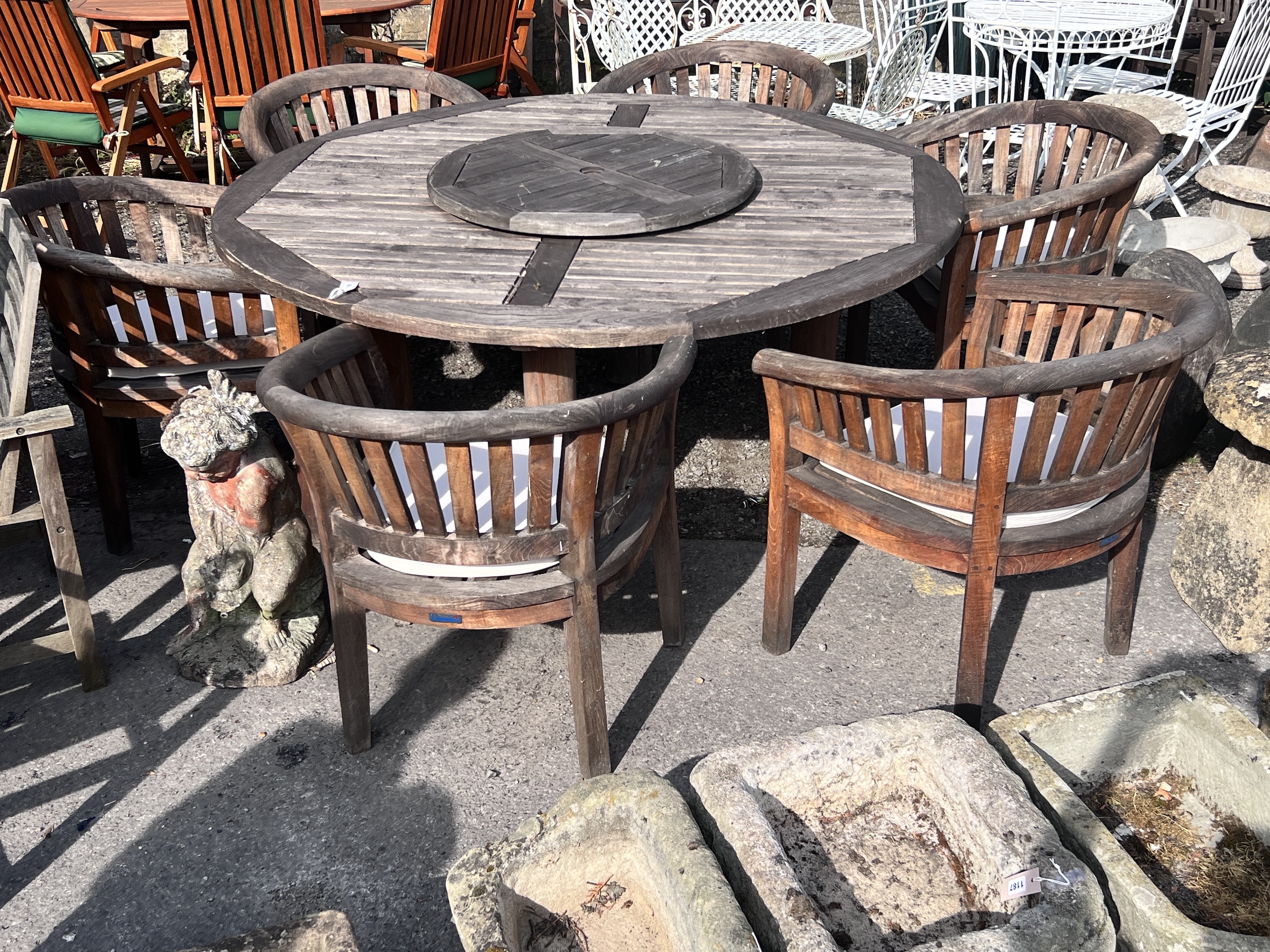 A large circular weathered teak garden table with Lazy Susan, diameter 180cm, height 75cm, together with six tub framed chairs with seat cushions